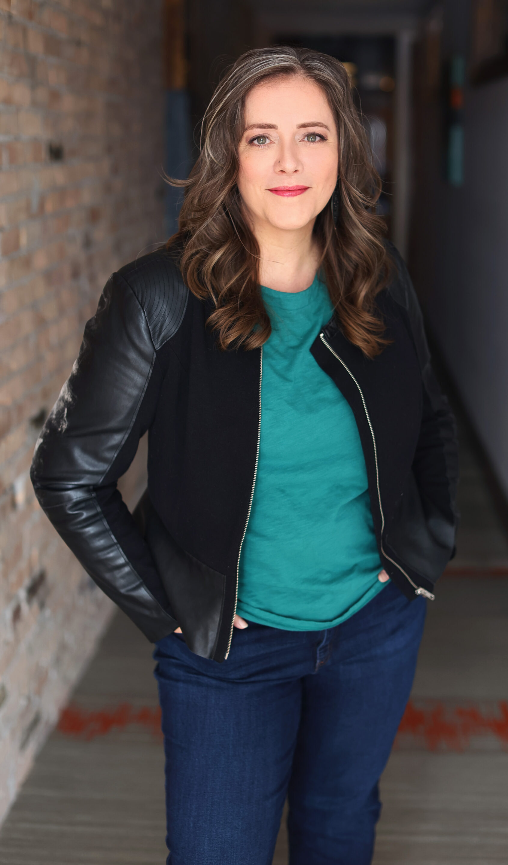 Angella Johnson standing in a hall wearing jeans, a green shirt and a black jacket.