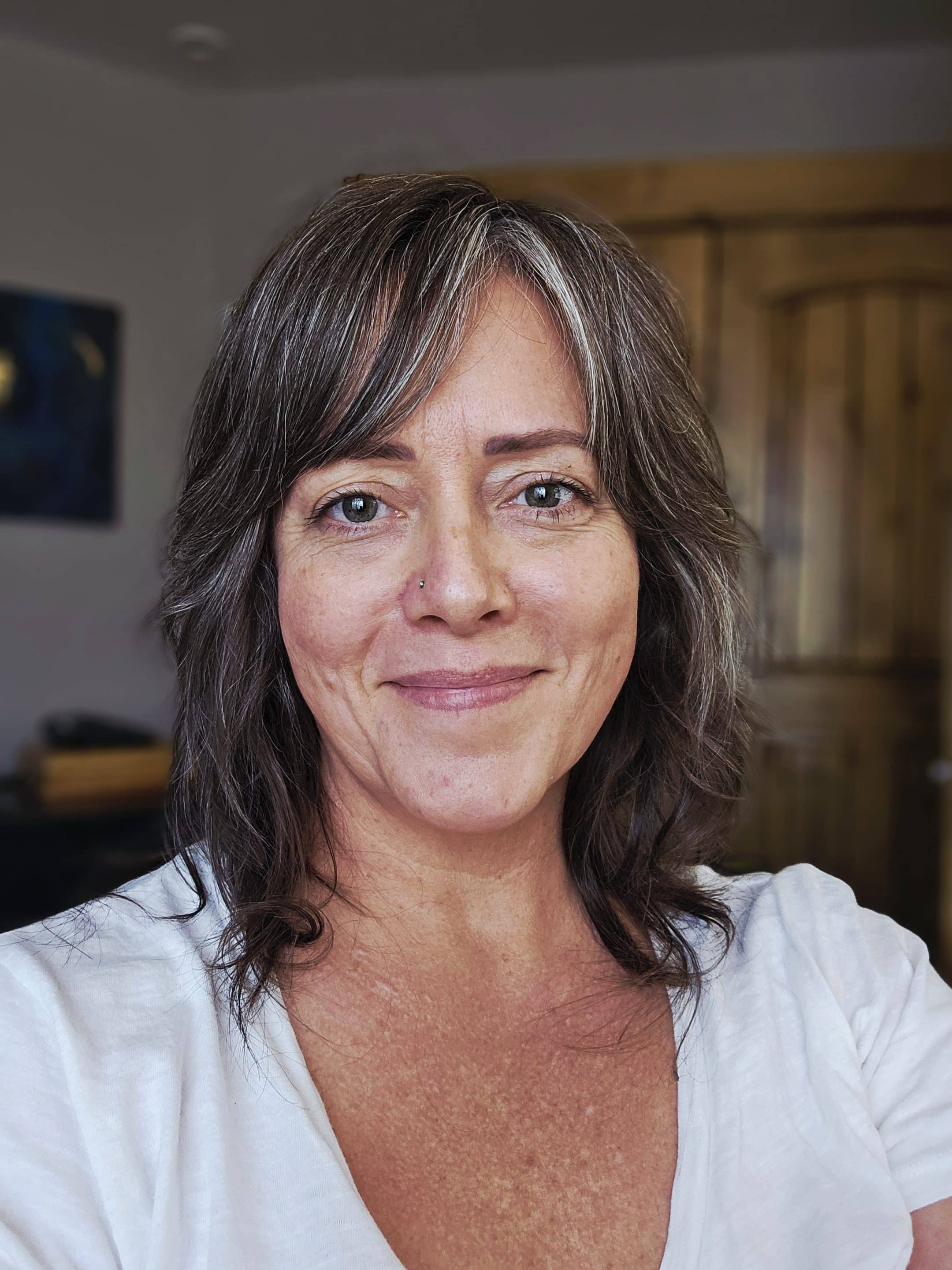 Angela Johnson August 2025 a photo of Angela Johnson in her home office wearing a white v-neck t-shirt.